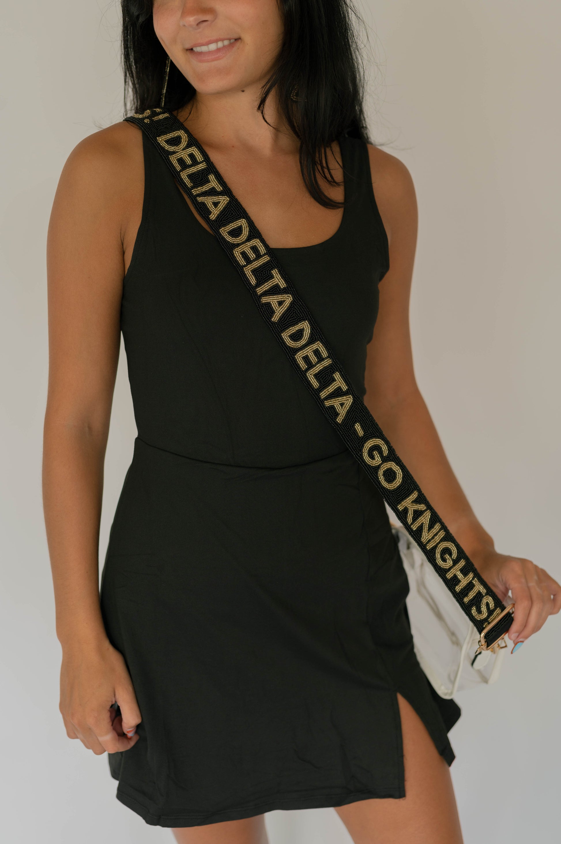Woman wearing a black dress with a 'Delta Delta Delta Go Knights' bag strap on a plain background