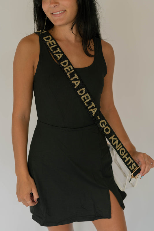 Woman wearing a black dress with a 'Delta Delta Delta Go Knights' bag strap on a plain background